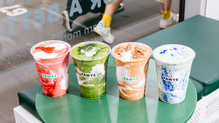 Four brightly coloured smoothies in a row on a green table. 