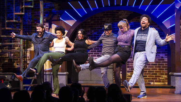 The cast dances on stage in a kickline.
