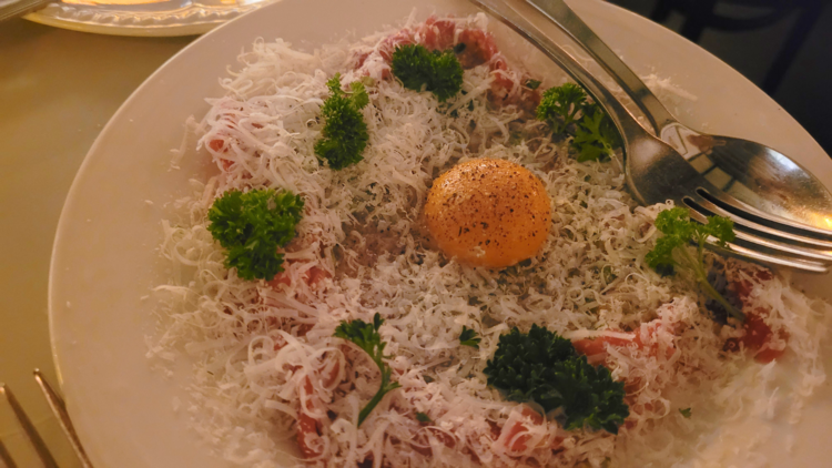 A plate of beef carpaccio with grated cheese and a confit egg yolk on top.