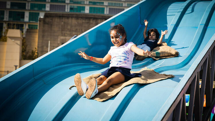 Two girls sliding down a blue long slide 