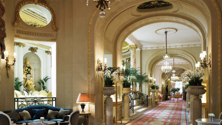 Hallway in The Ritz London with  sofa, hanging chandelier and an ornate rug. 