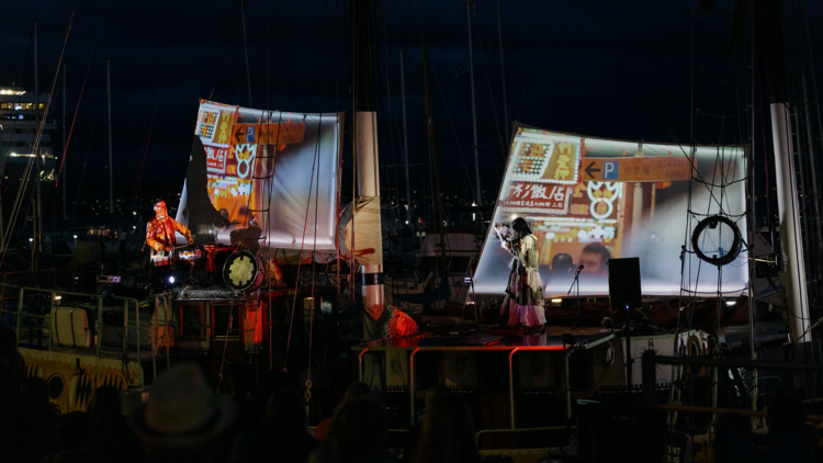 Performers on a boat with projections on the sales