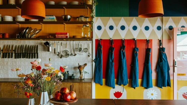 Colourful cooking and dining space with aprons, flowers and fruit.