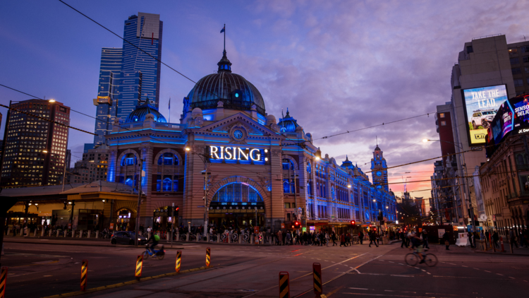The facade of Flinders Street Station lit in blue and emblazoned with the Rising logo