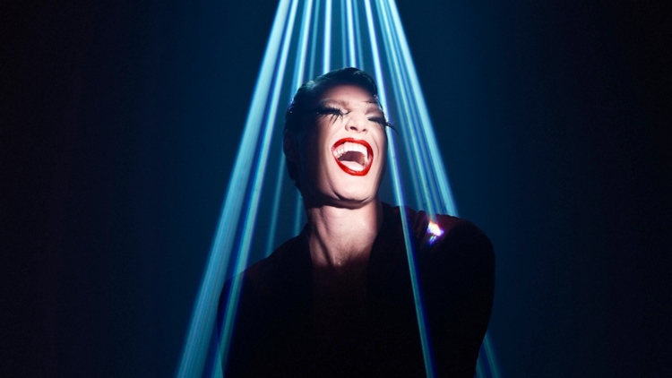 Reuben Kaye wearing red lipstick under rays of blue light