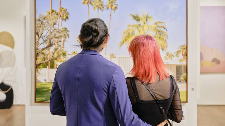 Two people look at artwork on a wall.