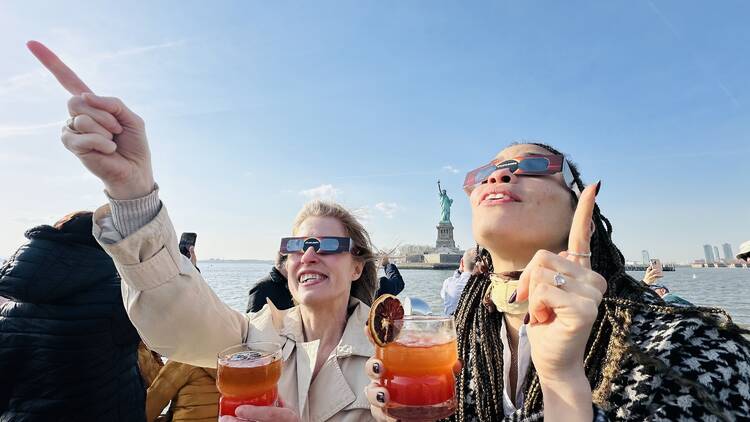 Two women, wearing eclipse glasses, on a boat cruise.