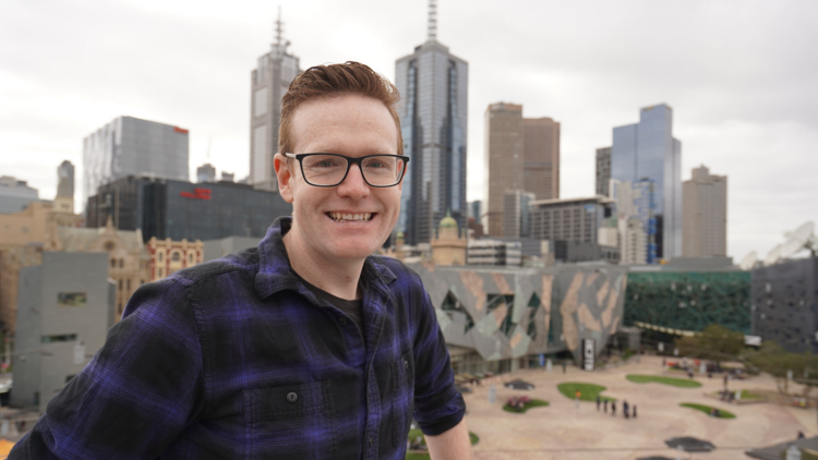 Julian O'Shea standing in front of Fed Square with the Melbourne skyline in the background