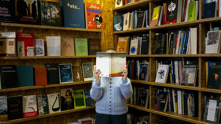 Beatriz Rodrigues, do Ursula Reading Club, com duas estantes atrás de si e um livro a tapar-lhe a cara
