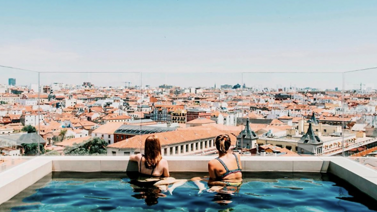 Two women in a rooftop terrace plunge pool overlooking the city.