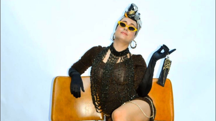 Thalia-Joan reclines on a chair wearing sunglasses, a headscarf, beads and gloves