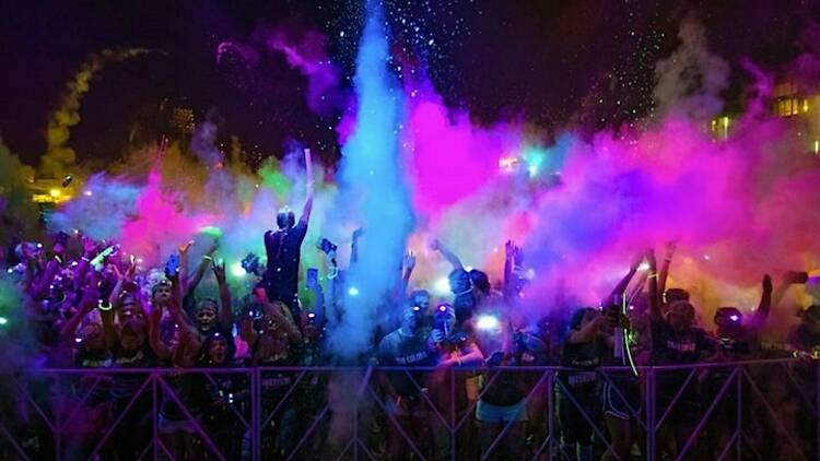 Splashes of colourful powder over a crowd of people at night time. 