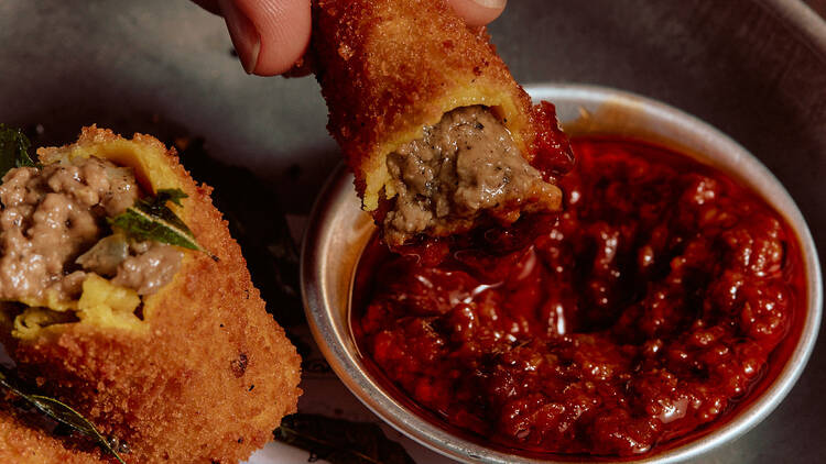 Diner dipping crumbed Sri Lankan-style croquettes into a fiery red sauce.