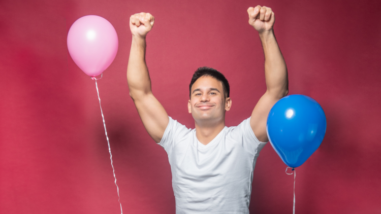 Josh Cake with arms raised, with a pink and blue balloon on either side