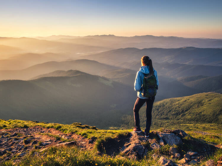 Girl on mountain peak with green grass looking at beautiful mountain valley in fog at sunset