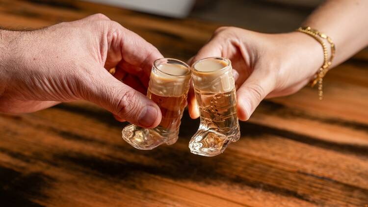 Two people cheersing with cowboy boot-shaped shot glasses.