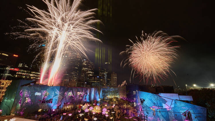 Fireworks over an illuminated Federation Square at night.