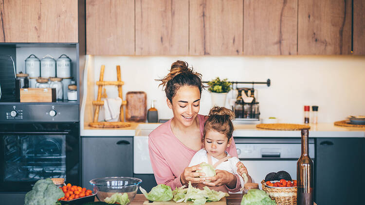 Woman having fun with her daughter while preparing salad in the kitchen.