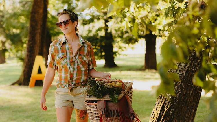 A woman in a check shirt walking with a full picnic basket.