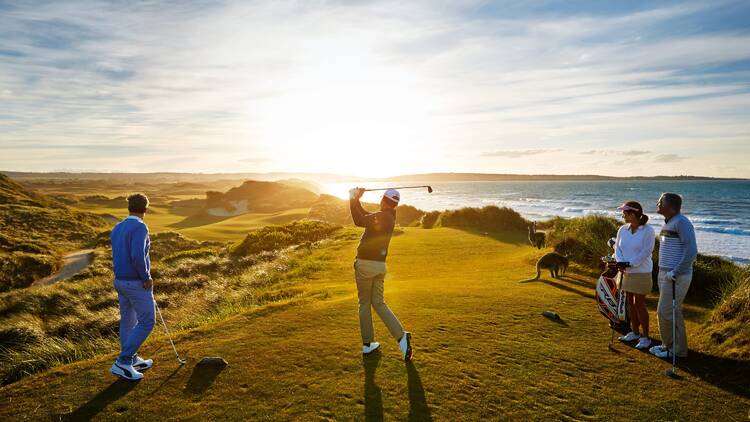 People golfing on a cliff at sunset