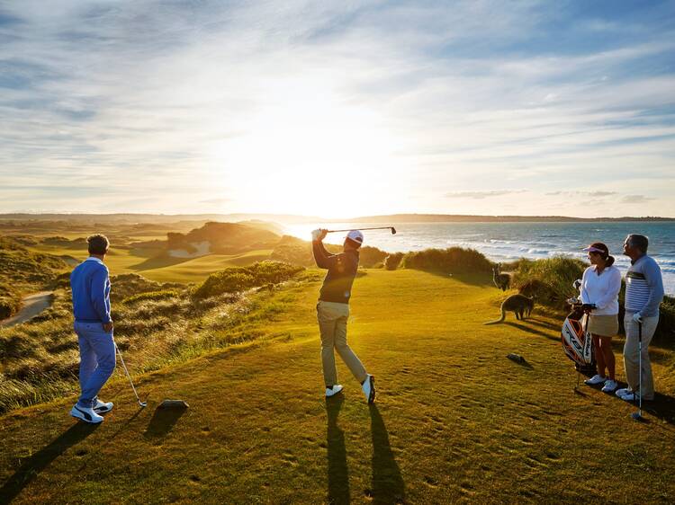 People golfing on a cliff at sunset