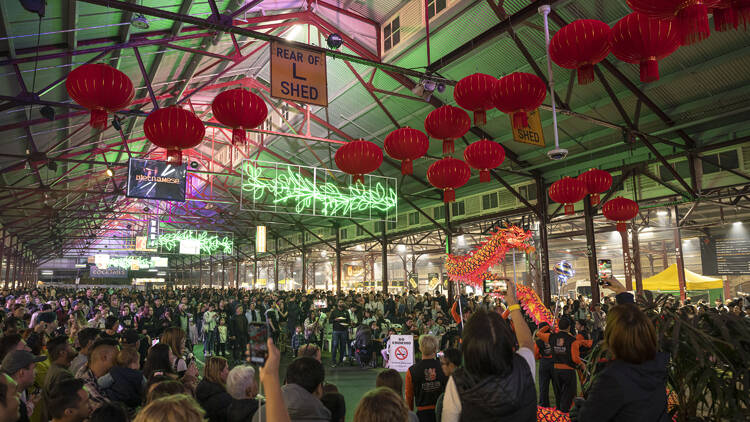 A crowded shed at Queen Victoria Market lit up with neon signs and red lanterns.