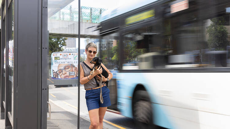 Dr Jennifer Kent holds her sausage dog and stands at a bus stop
