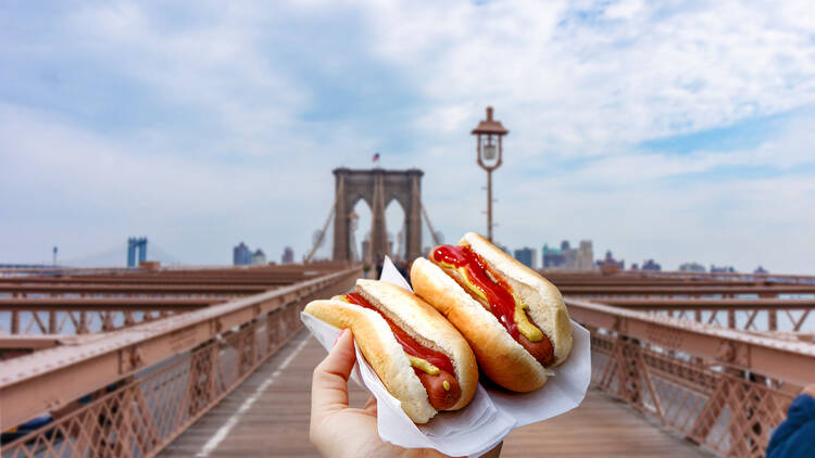 two hot dogs in front of the Brooklyn Bridge