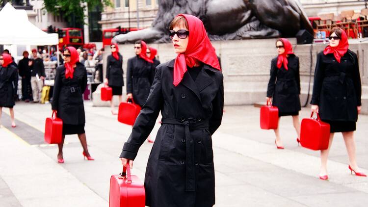 Women wearing red headscarves, black trench coats and big black sunglasses 