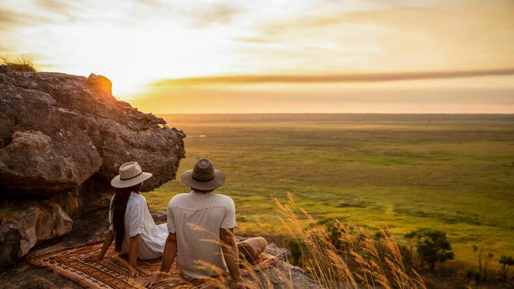 Two people overlooking green fields and a sunset