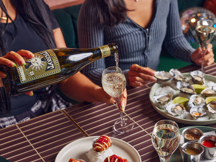 Woman pouring a glass of bubbly over a plate of oysters and other snacks with a friend. 