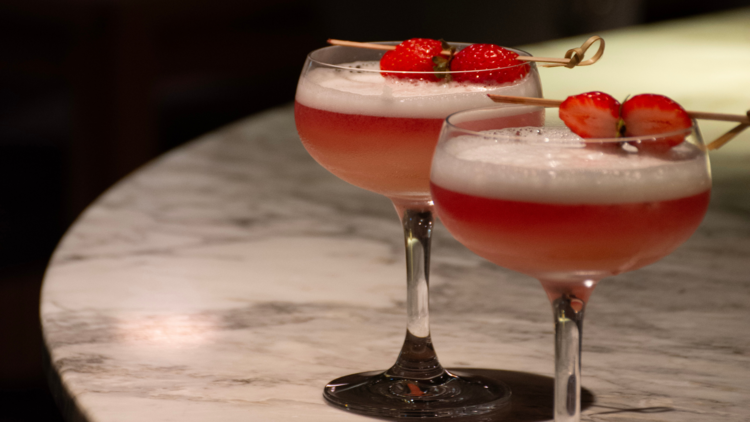 A picture of 2 pink cocktails with strawberries on top.