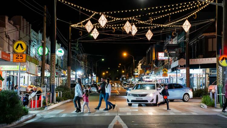 A family walking across the street under bright night lights in Lakemba.