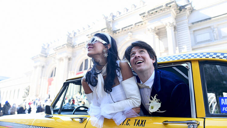 A couple sticks their heads out of a retro taxi window on their wedding day.