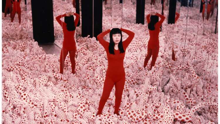 Yayoi Kusama in a red bodysuit, surrounded by one of her installations