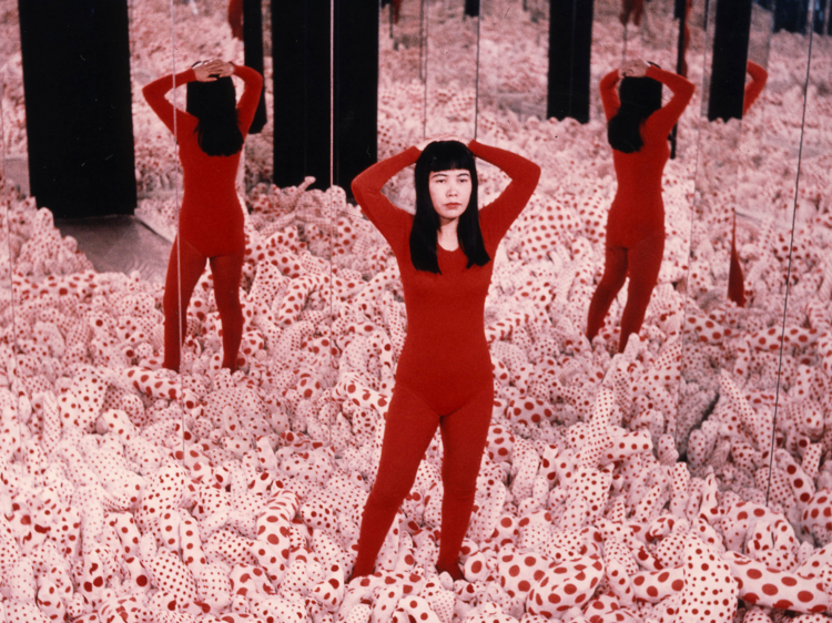 Yayoi Kusama in a red bodysuit, surrounded by one of her installations