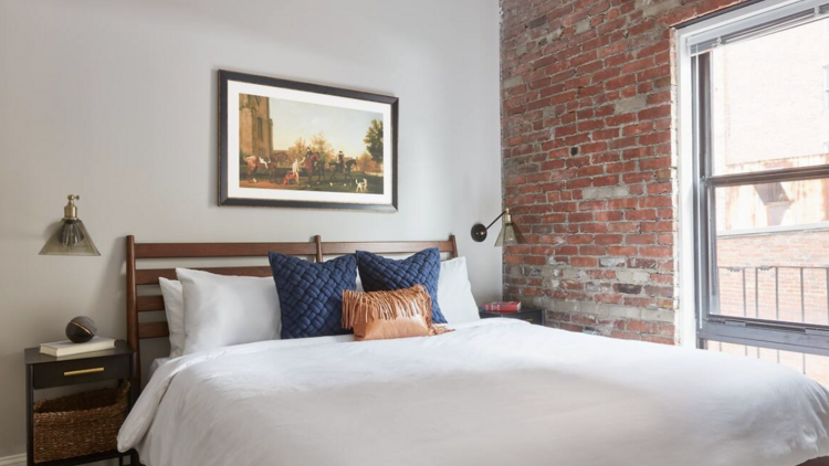 Rustic bedroom with exposed brick walls, and a large by the window. 