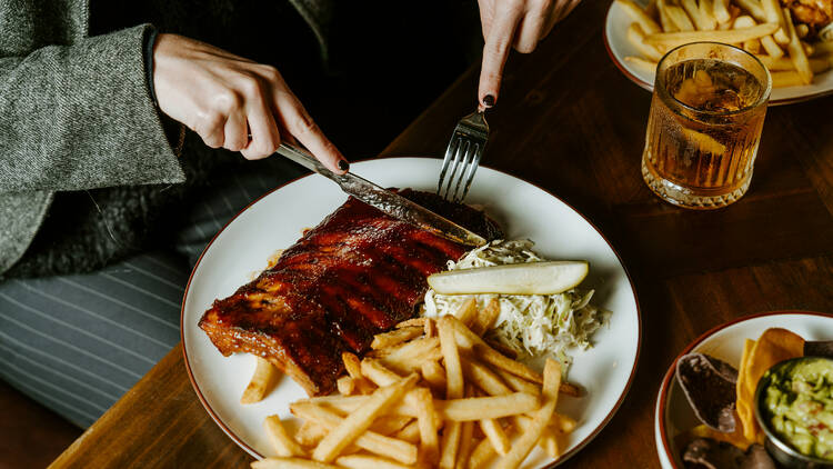 Diner cutting into ribs, chips and salad.