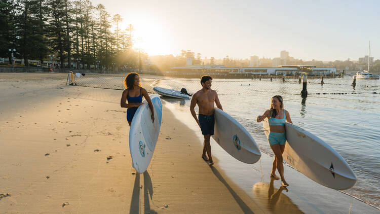 Three people walking on the beach holding surfboards