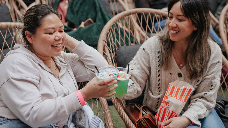 Two women hold cocktails at Rooftop Cinema Club.