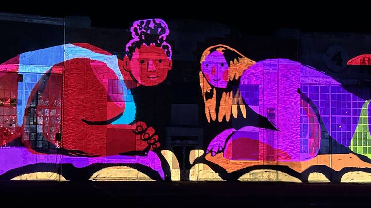 A digital projection of two people on the side of an airplane hangar.