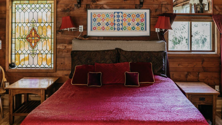 Bedroom with large bed covered in red velvet linen and two bedside tables. 