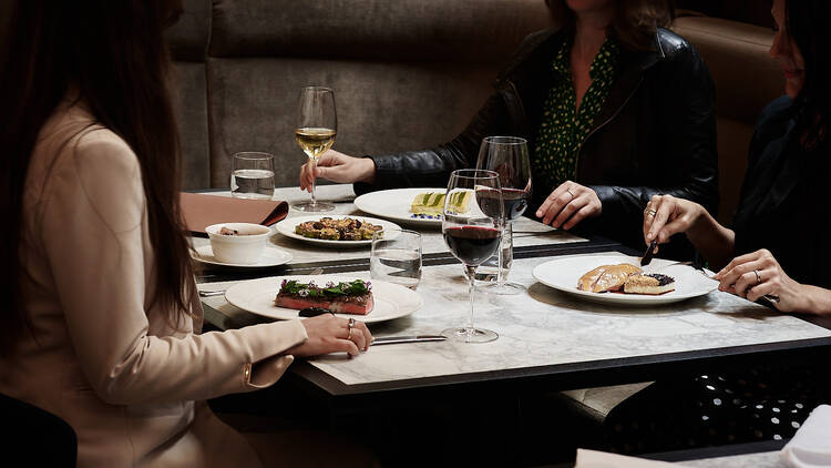 Diners sitting around a table with assorted dishes and glasses of wine at Luci.