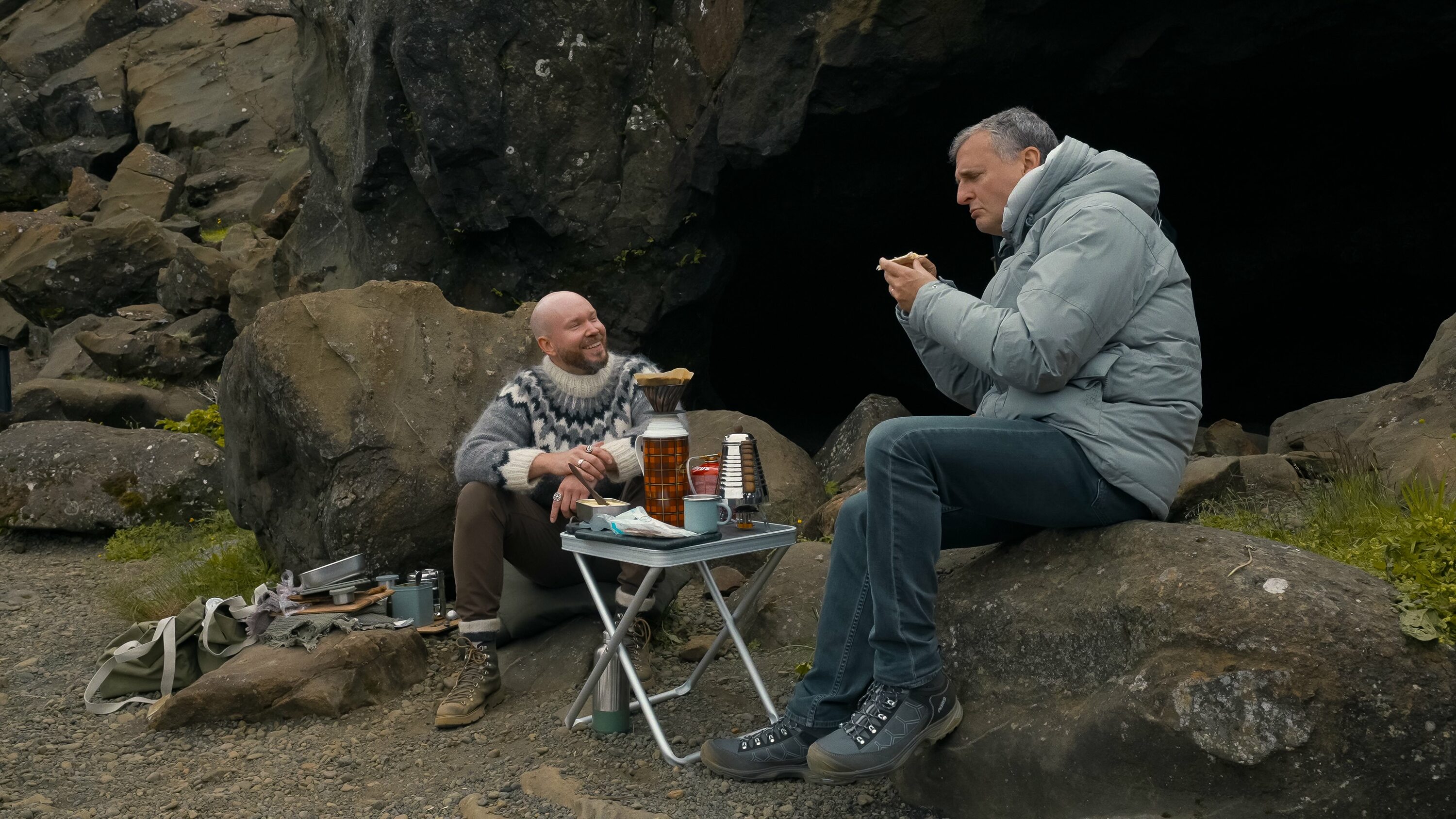 Two people sitting on rocks outside with food and drinks