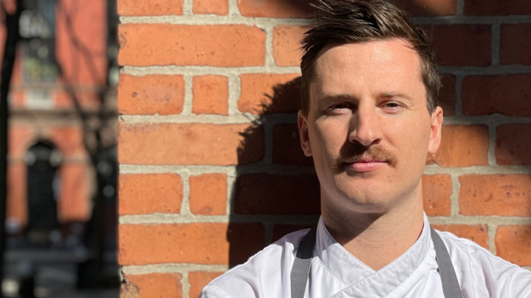 Chef Alistair McMurray posing for the camera in front of a brick wall.