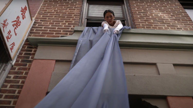 A woman pulls on a blue cloth flowing from a window.