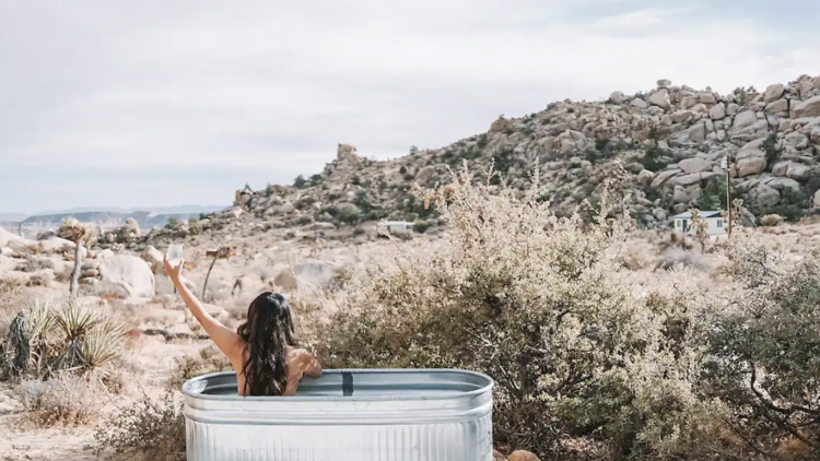 Woman in a cold plunge tub overlooking Mojave Desert. 