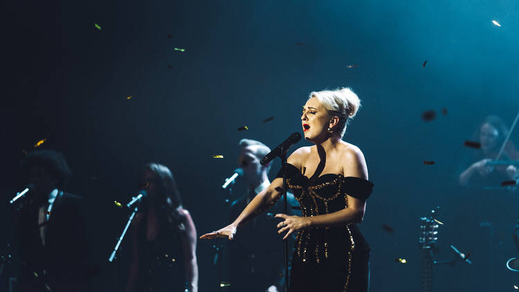 A blonde woman singing on a stage as confetti rains down around her.