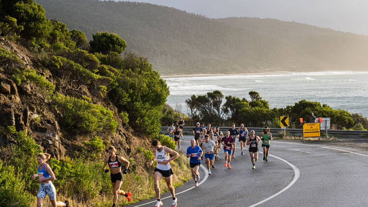 People running along the road with the ocean in the background. 