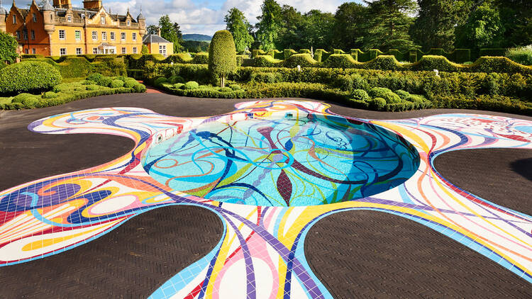 a colourful shaped pool outside a mansion and gardens